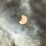 A captivating view of a solar eclipse partially covered by clouds in the sky.